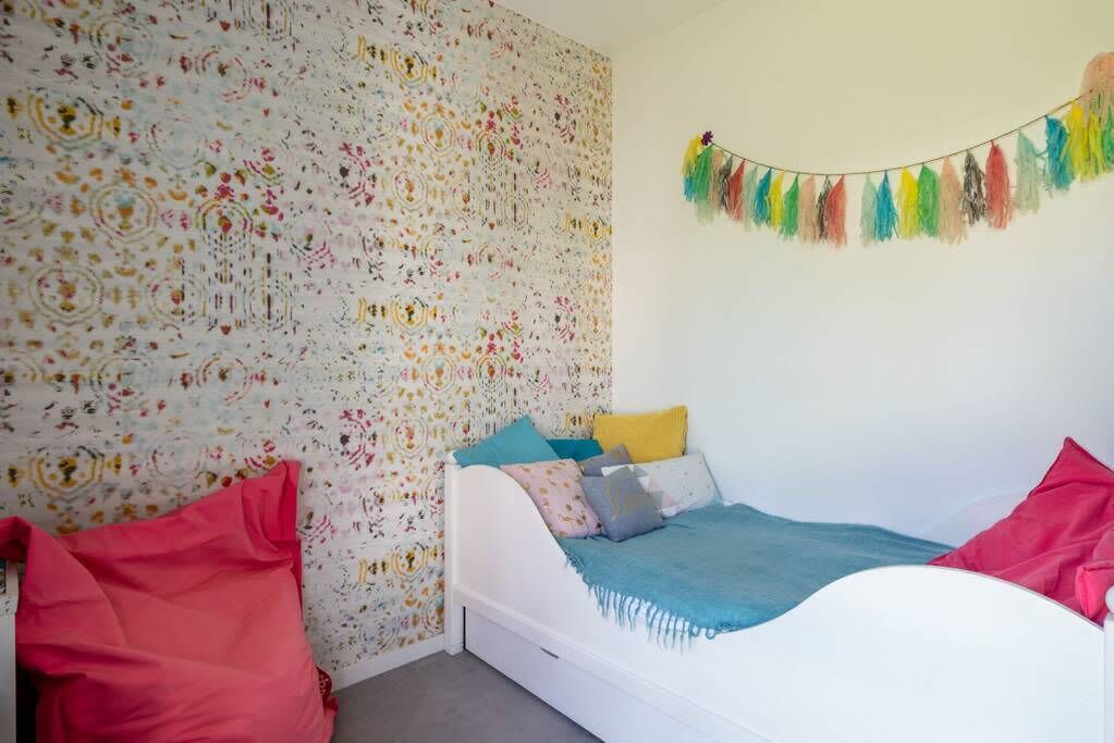 A bedroom with a patterned wallpaper, a bed with multiple pillows, and a colorful string decoration.