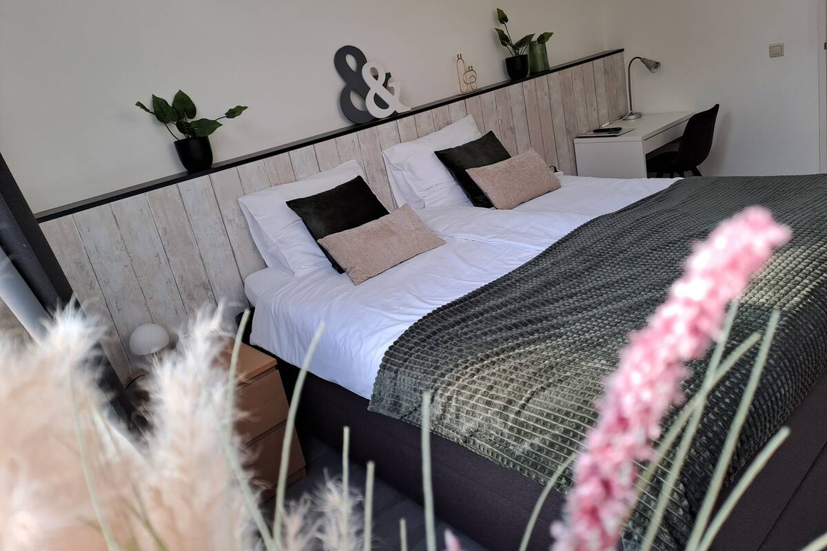 A neatly arranged bedroom with a bed, bedside tables, a desk, and decorative plants.