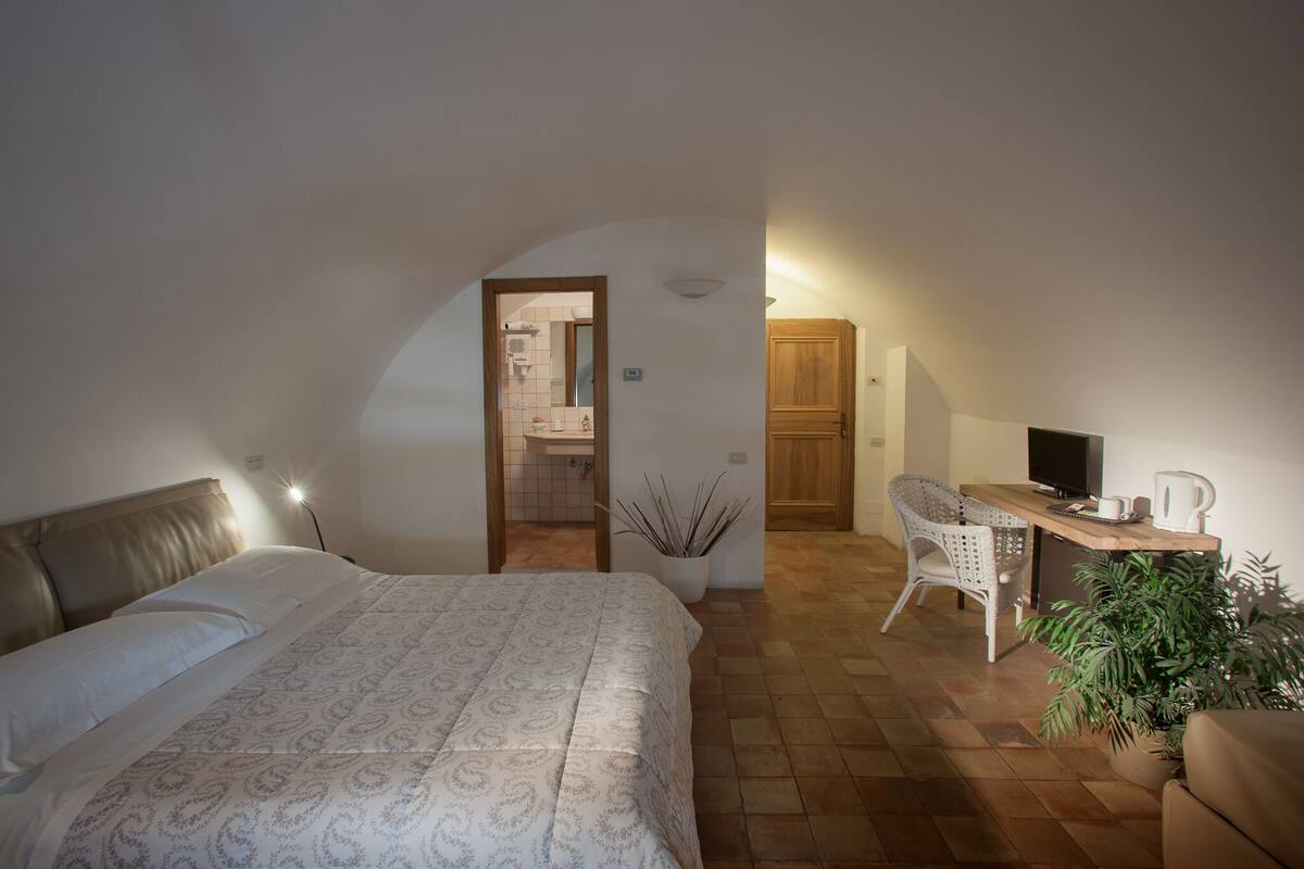 A bedroom with a bed, a desk, a chair, a television, and a potted plant.
