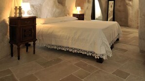 A bedroom with a stone archway, a bed with a white bedspread, a wooden nightstand with a lamp, and a mirror on the wall. - Ai Terrazzini (Matera)