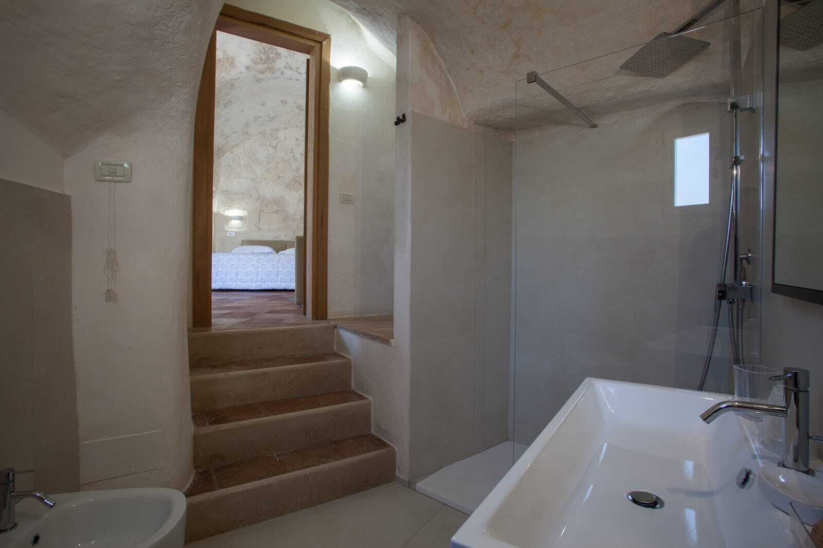 Une salle de bain avec une douche, un lavabo et des toilettes. Un escalier mène à une autre pièce.