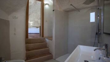 Une salle de bain avec une douche, un lavabo et des toilettes. Un escalier mène à une autre pièce.