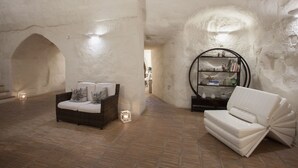 A cozy interior with a wicker sofa, a white cushioned chair, and a round mirror on a textured wall. - Ai Terrazzini (Matera)