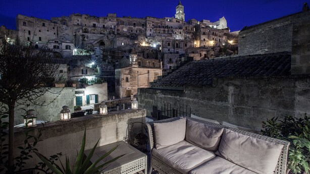 A terrace with a cushioned seating area overlooking a historic cityscape at night. - Ai Terrazzini (Matera)