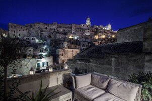 Una terrazza con zona salotto imbottita che si affaccia su un centro storico illuminato di notte.