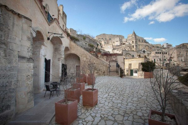 A courtyard with stone flooring, outdoor seating, and a view of historic buildings in the background. - Ai Terrazzini (Matera)