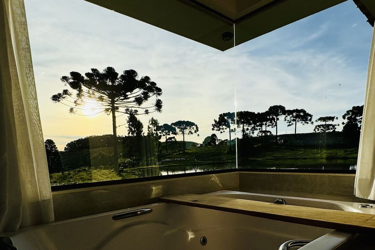 Une salle de bain moderne dotée d’une grande baignoire, d’un espace douche et offrant une vue sur un paysage arboré.