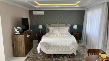 A bedroom with a tufted headboard bed, two bedside tables with lamps, a wooden dresser, a fluffy rug, and a dining table with a cake.