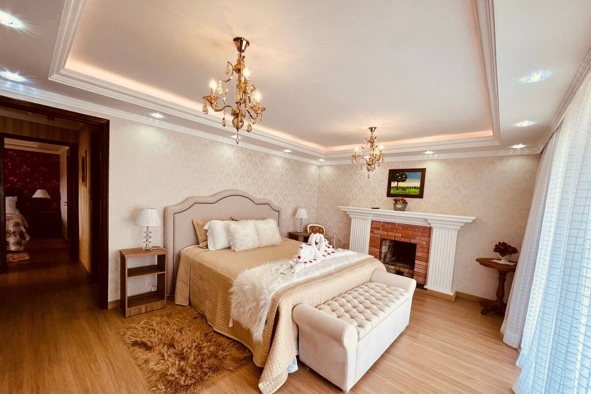Une chambre spacieuse avec un grand lit, une cheminée et un lustre.