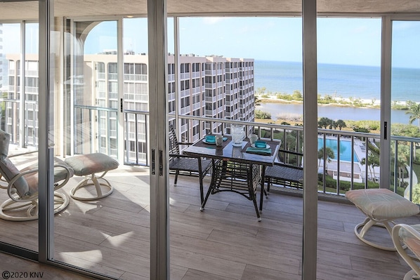 A balcony with a table and chairs, overlooking a beach and ocean.