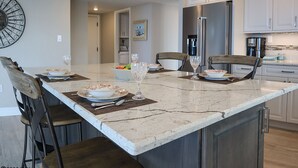 Une cuisine moderne dotée d’un grand îlot central, d’appareils électroménagers en acier inoxydable et d’un coin repas avec des chaises et une table dressée pour le repas.