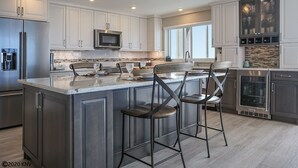 Une cuisine moderne dotée d’un grand îlot central, d’appareils électroménagers en acier inoxydable et de tabourets de bar.
