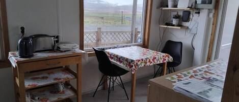 Una habitación con un escritorio de madera, una silla, un ventanal con vistas al paisaje y un estante con objetos.