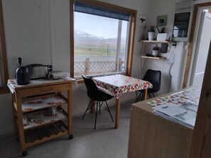A room with a wooden desk, a chair, a window with a view of a landscape, and a shelf with items.