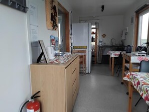 Eine kleine Küche mit einem Kühlschrank, einem Esstisch mit einer blumigen Tischdecke und einem Feuerlöscher.