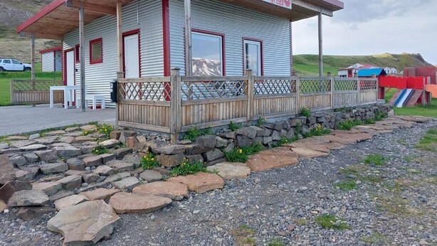 Un petit bâtiment doté d’une terrasse en bois, d’un chemin en pierre et d’un panneau indiquant l’emplacement des toilettes.