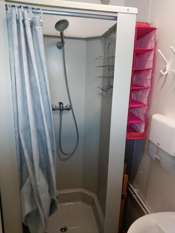Un box de ducha con ducha, cortina y estante rosa.