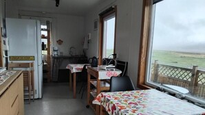 Une pièce comprenant un coin cuisine, une table à manger recouverte d’une nappe à motifs floraux et offrant une vue sur la mer grâce à de grandes fenêtres.