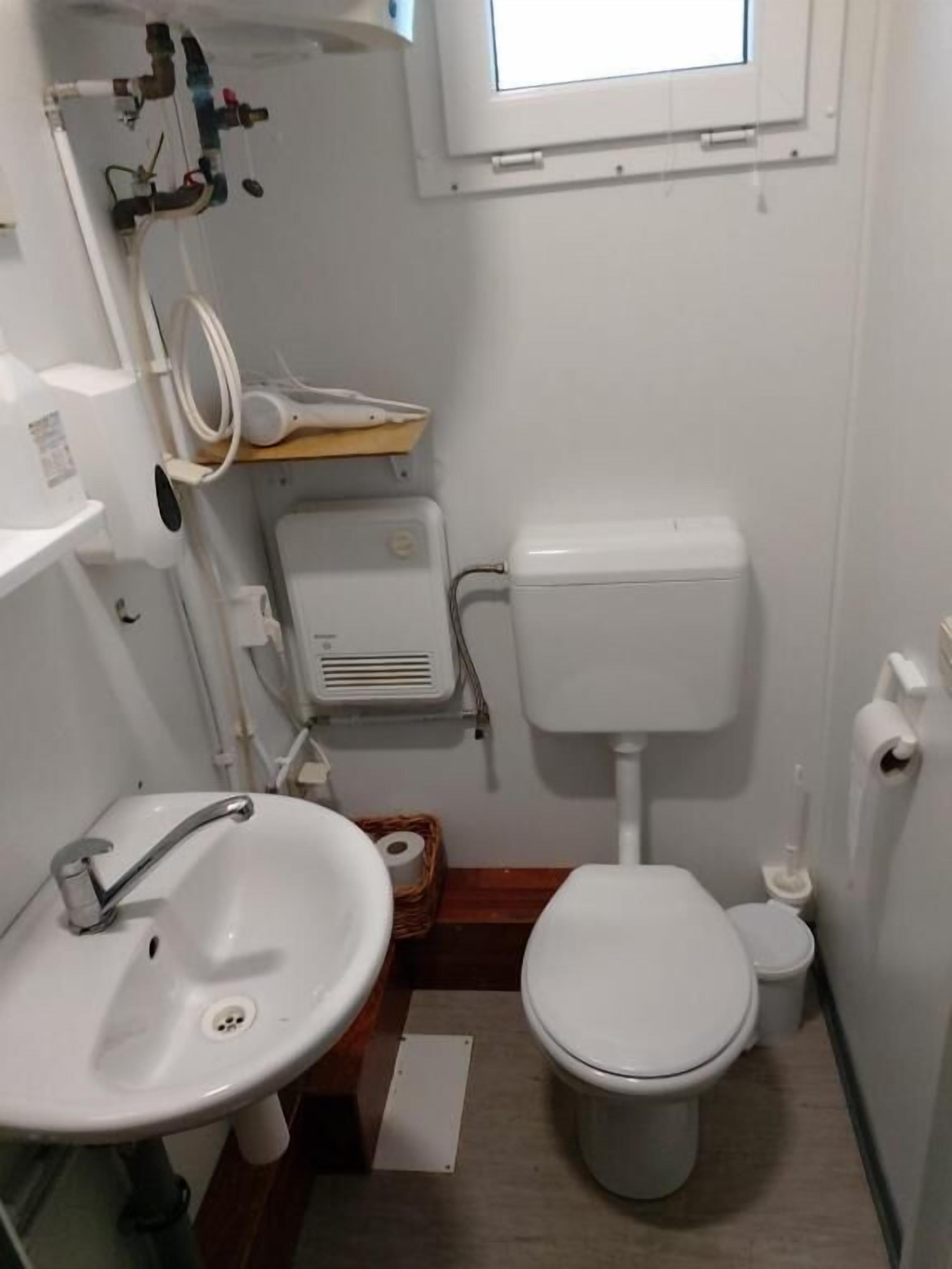 A small bathroom with a white sink, toilet, and a window above the toilet.