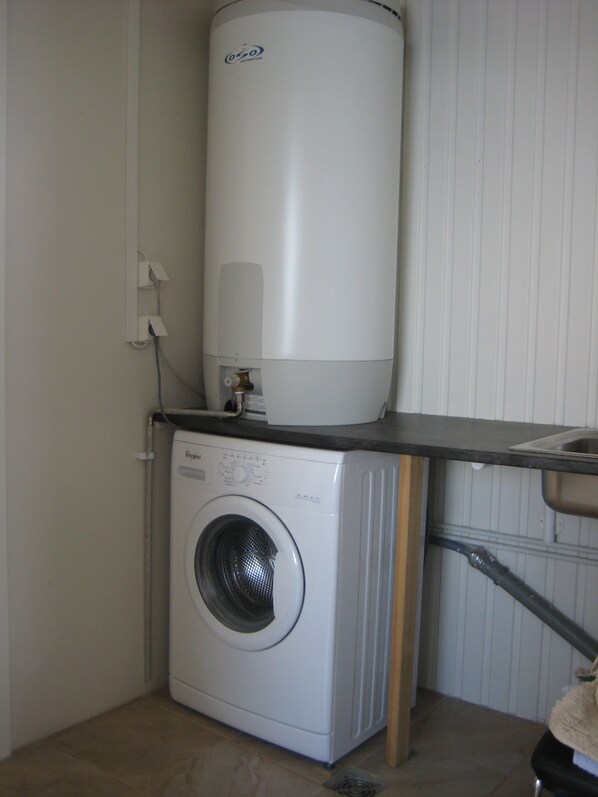 A compact laundry area with a front-loading washing machine and a vertical water heater. - Ásbrandsstaðir Cottage (Vopnafjordur)