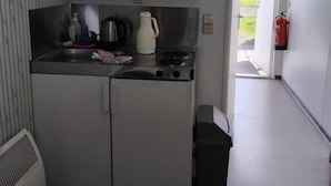 Une petite cuisine équipée avec une cuisinière, une bouilloire et un évier, une petite poubelle et une porte donnant sur un espace extérieur.