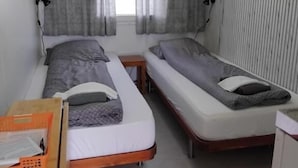 Une chambre avec deux lits simples, une petite table, une chaise et une fenêtre avec des rideaux.