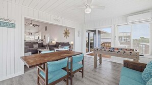 Ein Zimmer mit Holztisch, Stühlen, einer Couch, einem Kicker und einem Deckenventilator.