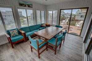 Relax in this serene sunroom with a comfortable sofa set and a wooden table surrounded by large windows.
