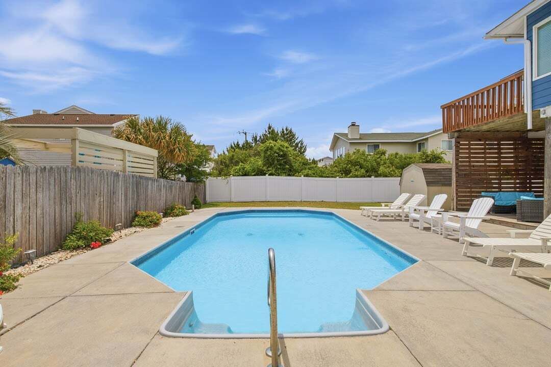 Una piscina rectangular con una baranda de seguridad metálica en el centro, rodeada por un solárium de hormigón.