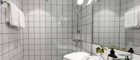 A modern bathroom with white tiled walls, a black tiled floor, a glass shower enclosure, a white sink with a mirror, and a small plant on the counter.