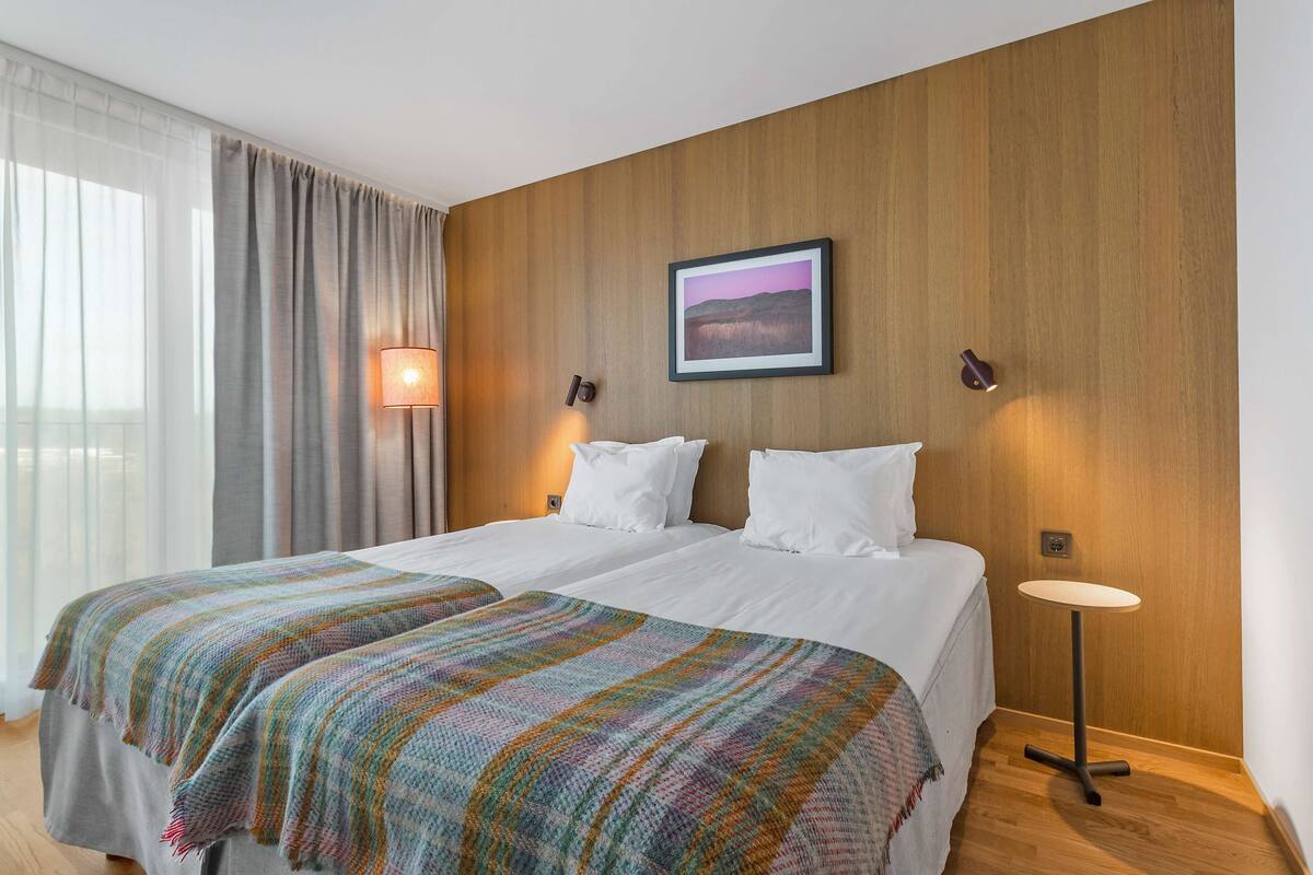 A double bed with a colorful blanket, a bedside table, and a wall-mounted lamp.