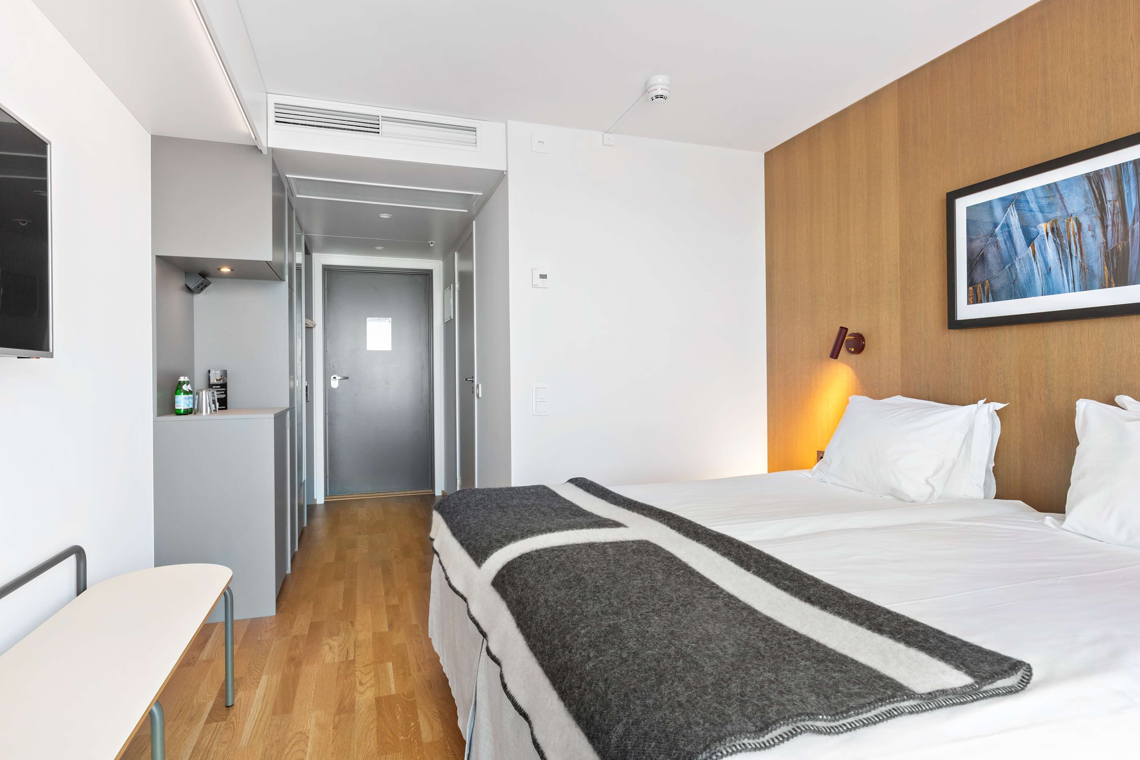 Ein Hotelzimmer mit Bett, Schreibtisch, Stuhl, Kleiderschrank und einem Gemälde an der Wand.