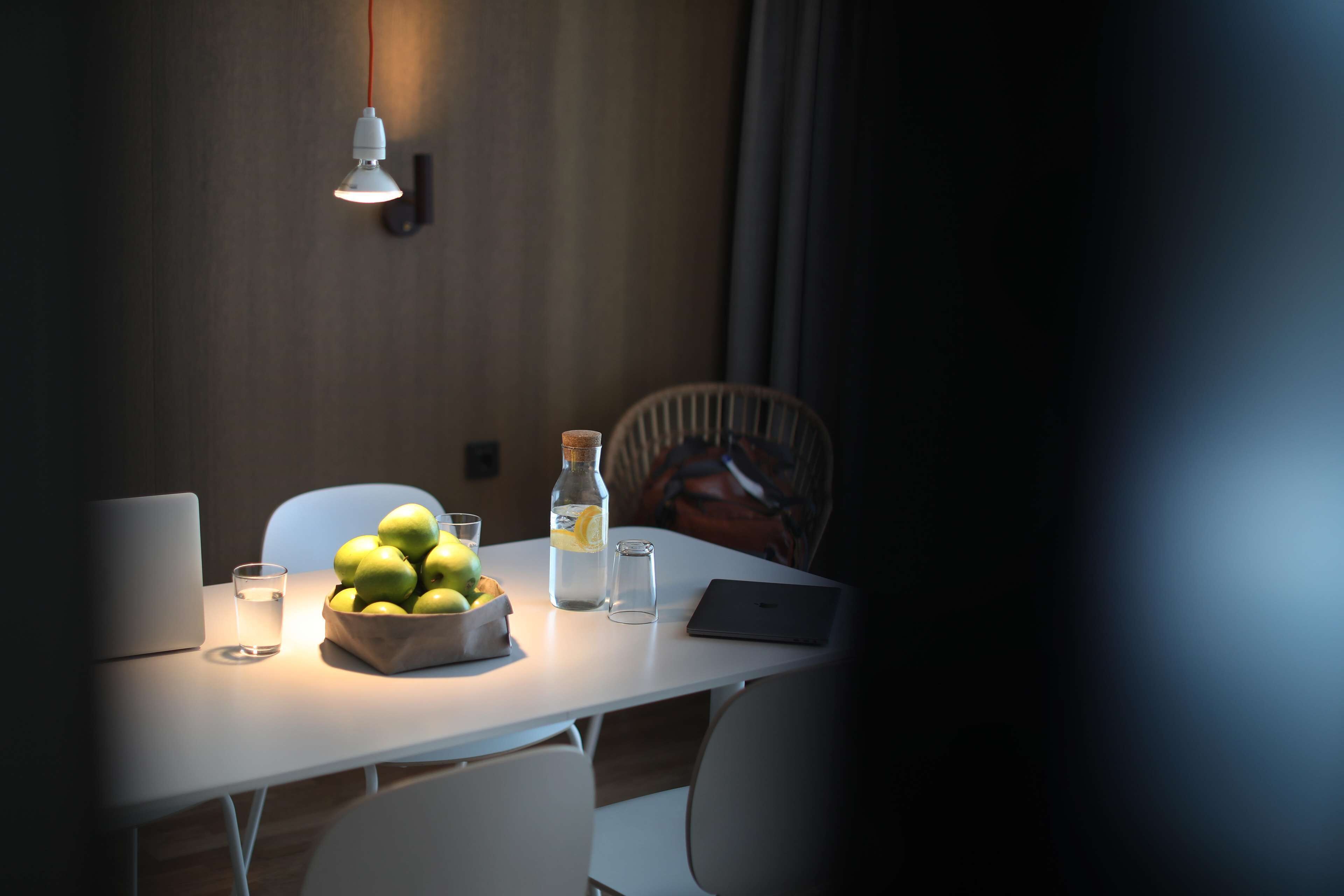 Ett matbord med en bärbar dator, en skål med frukt, en vattenflaska och ett glas.