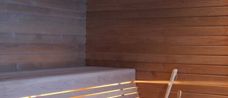 A wooden bench with a white bucket and a spoon, set against a wall with horizontal wooden panels.