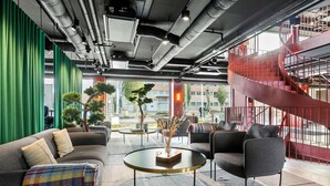 Un área de estar moderna con un sofá, sillones y una mesa de centro. Se observa una escalera con barandas rojas y vistas al exterior.