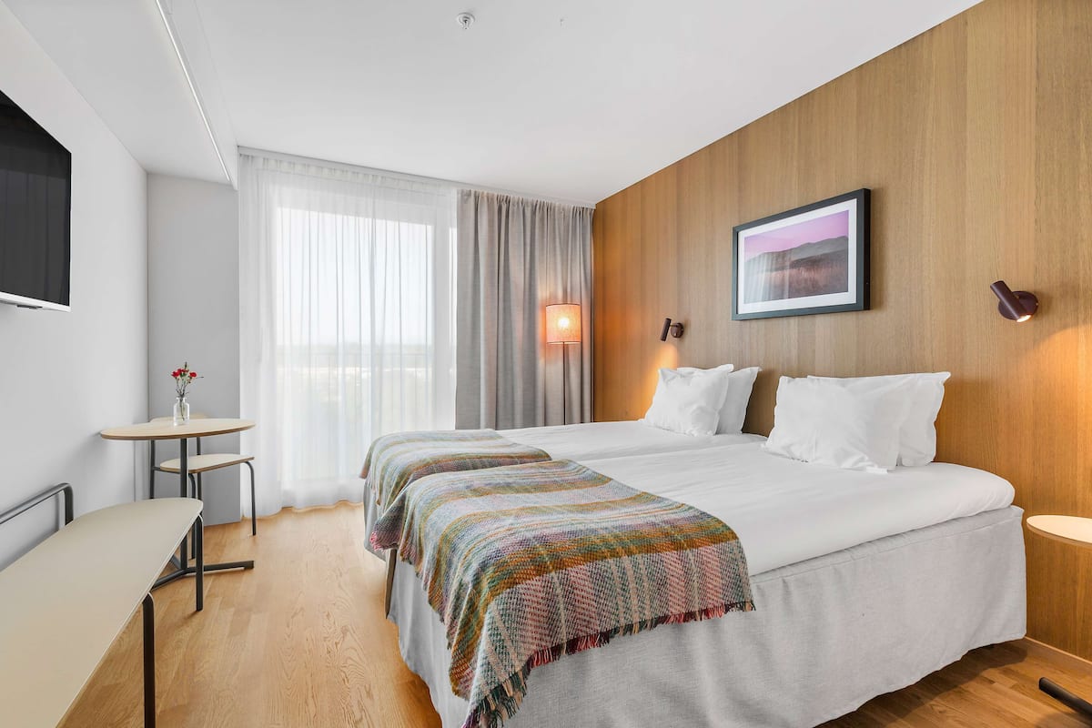 A hotel room with two beds, a small table, a TV, and a lamp.
