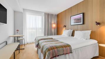 Hotellihuone, jossa on kaksi sänkyä, pieni pöytä, televisio ja lamppu.