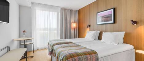 Una habitación de hotel con dos camas, una mesita, un televisor y una lámpara.