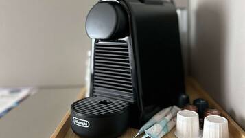 Una cafetera negra con el logotipo de Delonghi, una bandeja con cápsulas de café y un pequeño recipiente con crema.