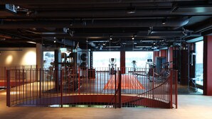 Un gimnasio interior con equipamiento de ejercicio, una pista de atletismo roja y una pared de vidrio que ofrece vistas al exterior.