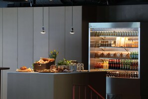 A bar area with a refrigerator stocked with beverages, a wooden box with pastries, and hanging lights. - Best Western Plus Ten Hotel (Upplands Vasby)