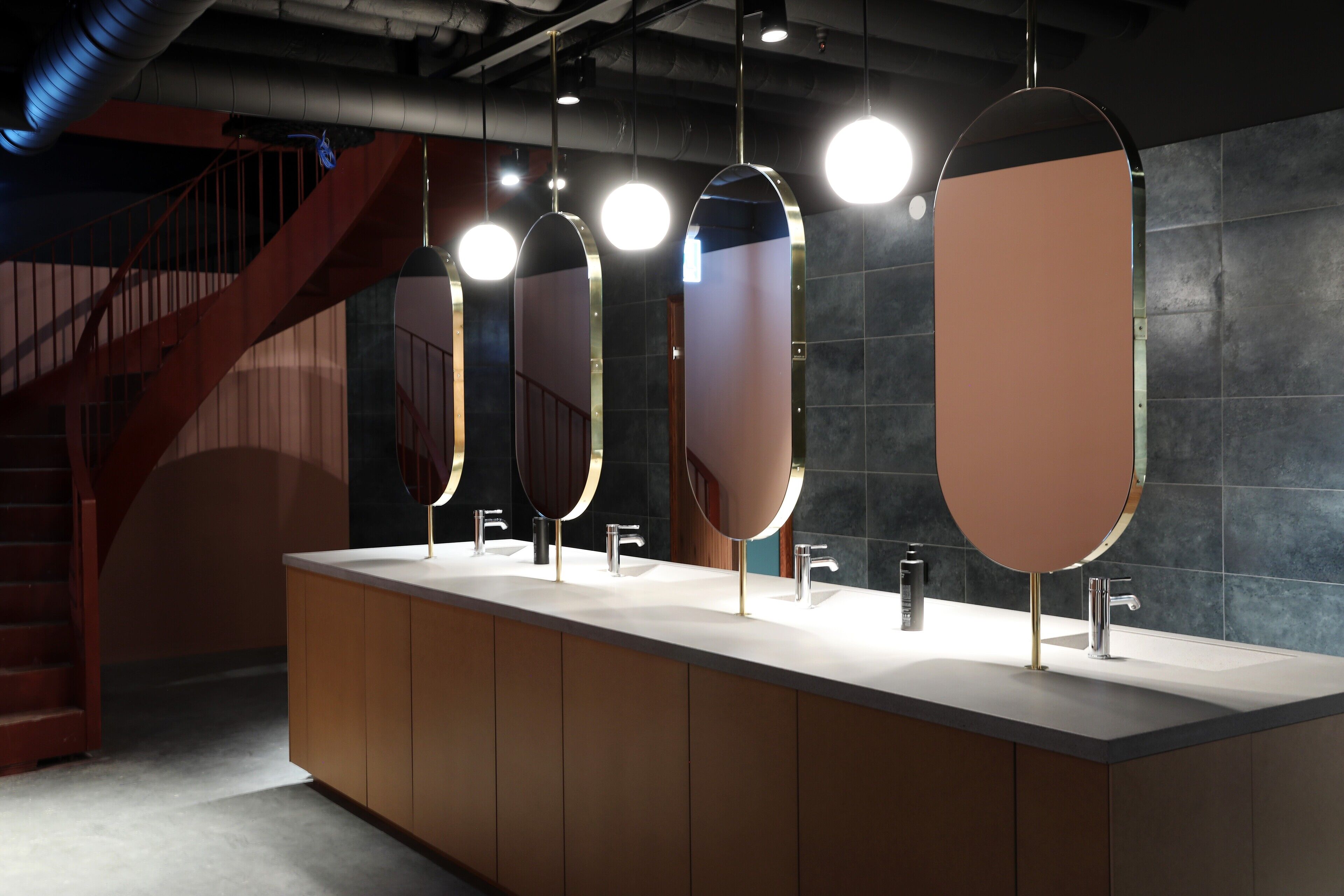 Un baño moderno con un lavabo alargado, varios lavamanos y una escalera al fondo.