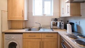 Eine kleine Küche mit Waschmaschine, Spüle, Fenster und Herd.