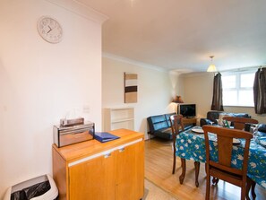 A compact living space with a kitchenette, a dining area with a table and chairs, a television, and a clock on the wall.