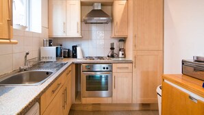 Eine kompakte Küche mit Holzschränken, einem Edelstahlbackofen, einer Spülmaschine und einer Kaffeemaschine.