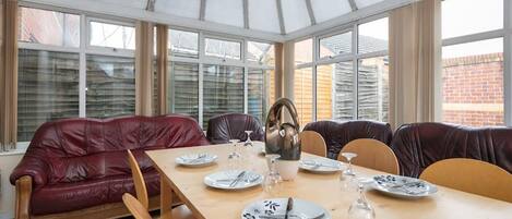 A conservatory with a dining table set for four, surrounded by leather sofas and chairs.