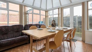 Une véranda avec une table en bois dressée pour le repas, entourée de chaises.