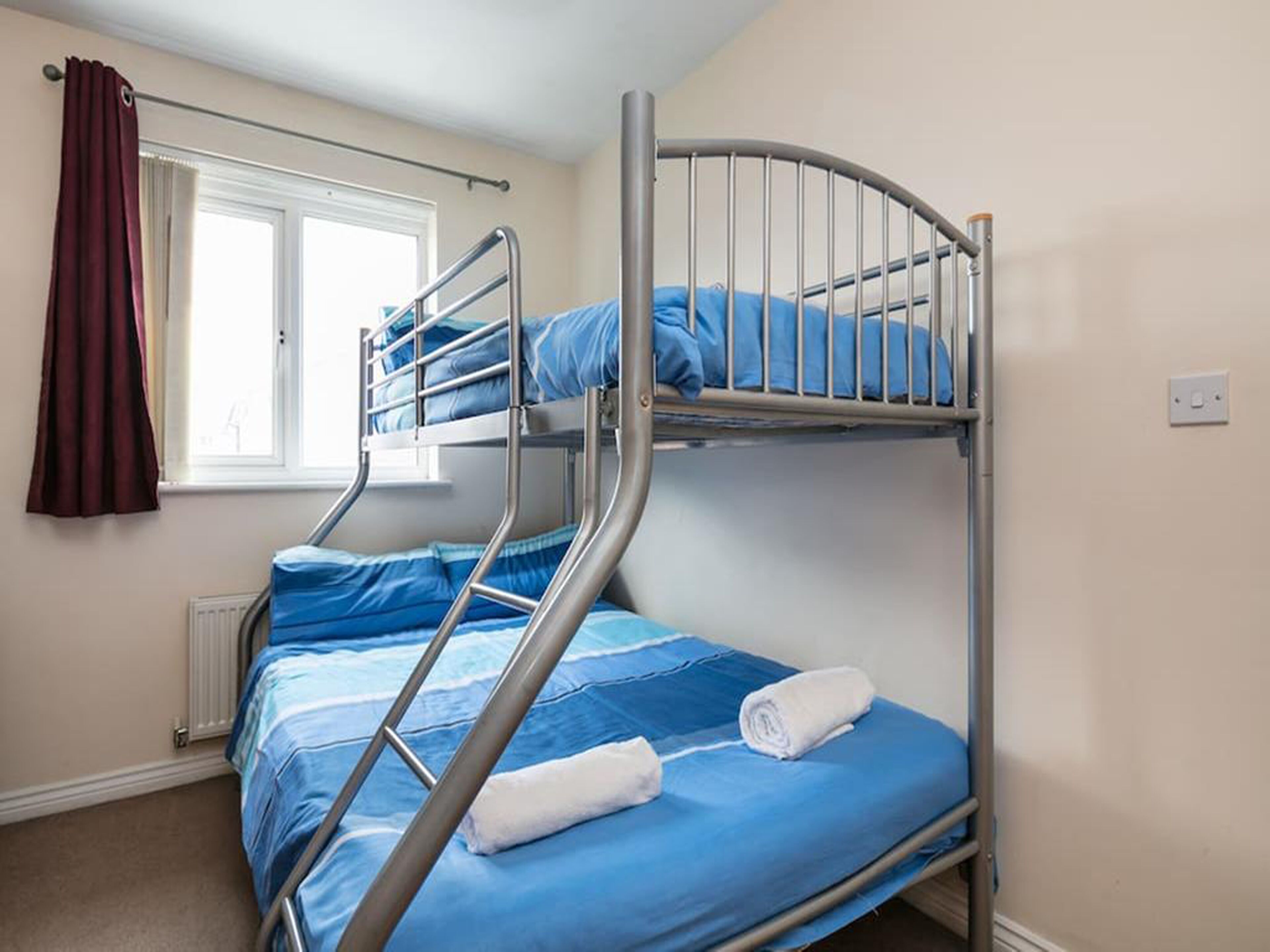 A bunk bed with blue bedding and a window with curtains.