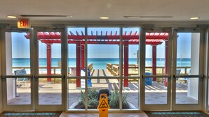 A beach view through a glass door with a red pergola and a caution sign on the floor.