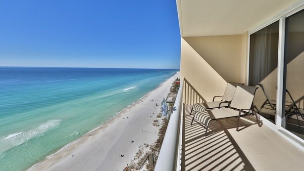 A balcony with two chairs overlooking a beach and the ocean.